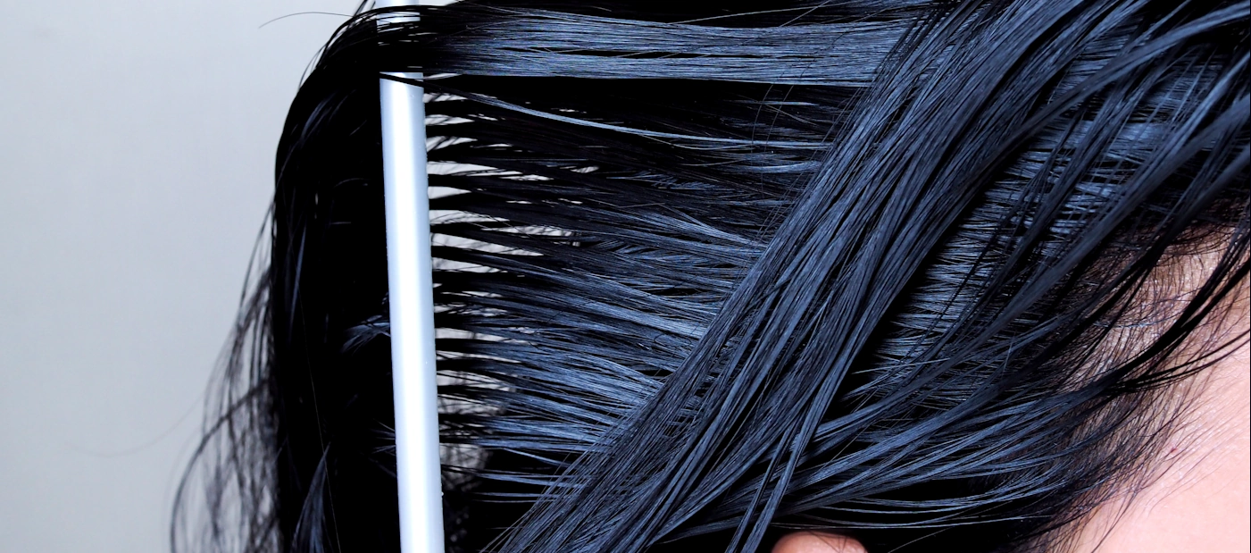 A comb dragging through wet, oily-looking dark hair, the strands clumped and flattened at the root.